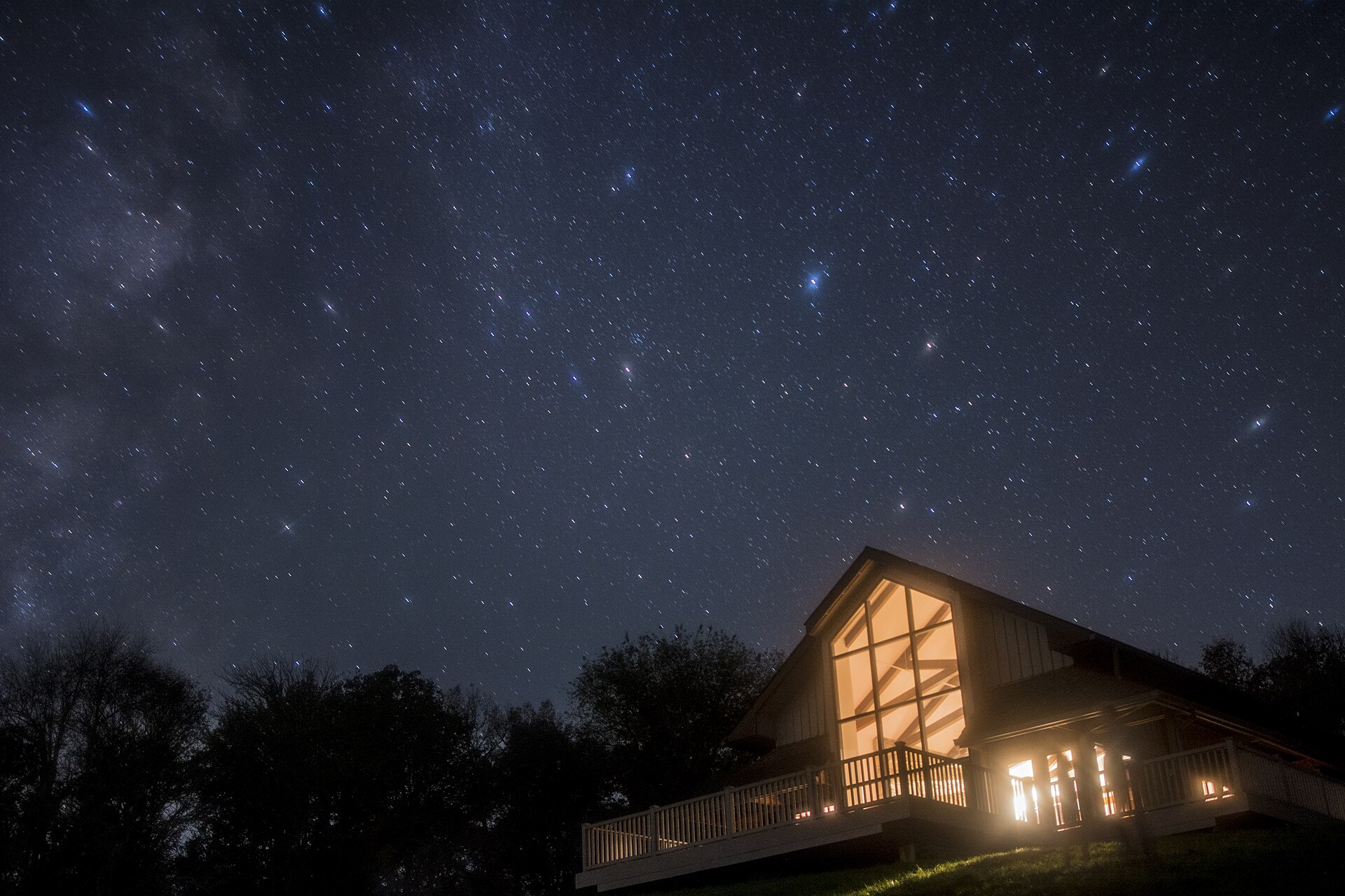 The Milky Way over a lit lodge under a star field